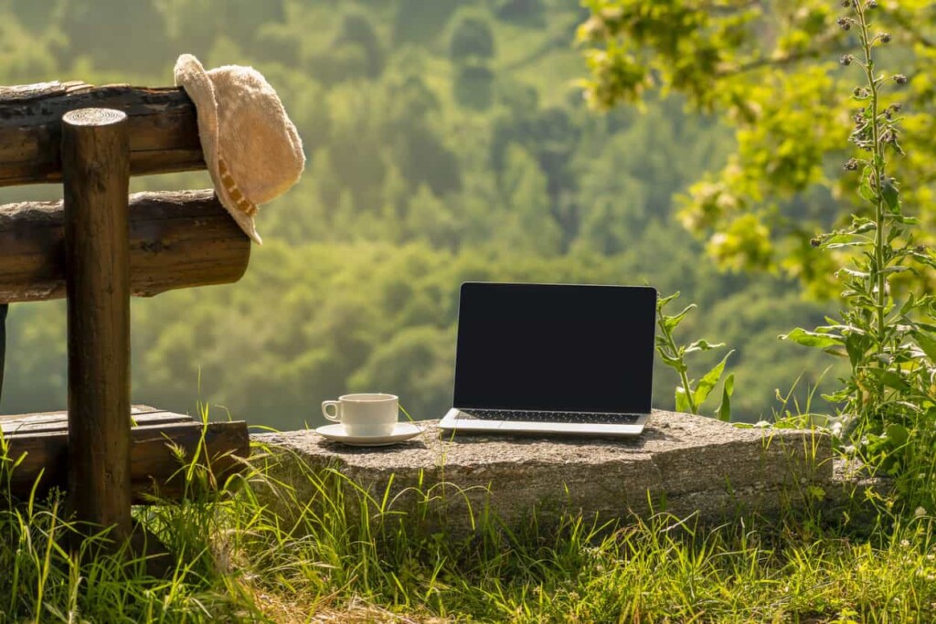 A laptop set up on with a cup of coffee, overlooking a scenic countryside view.